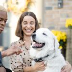 Multiracial couple caress dog near their house